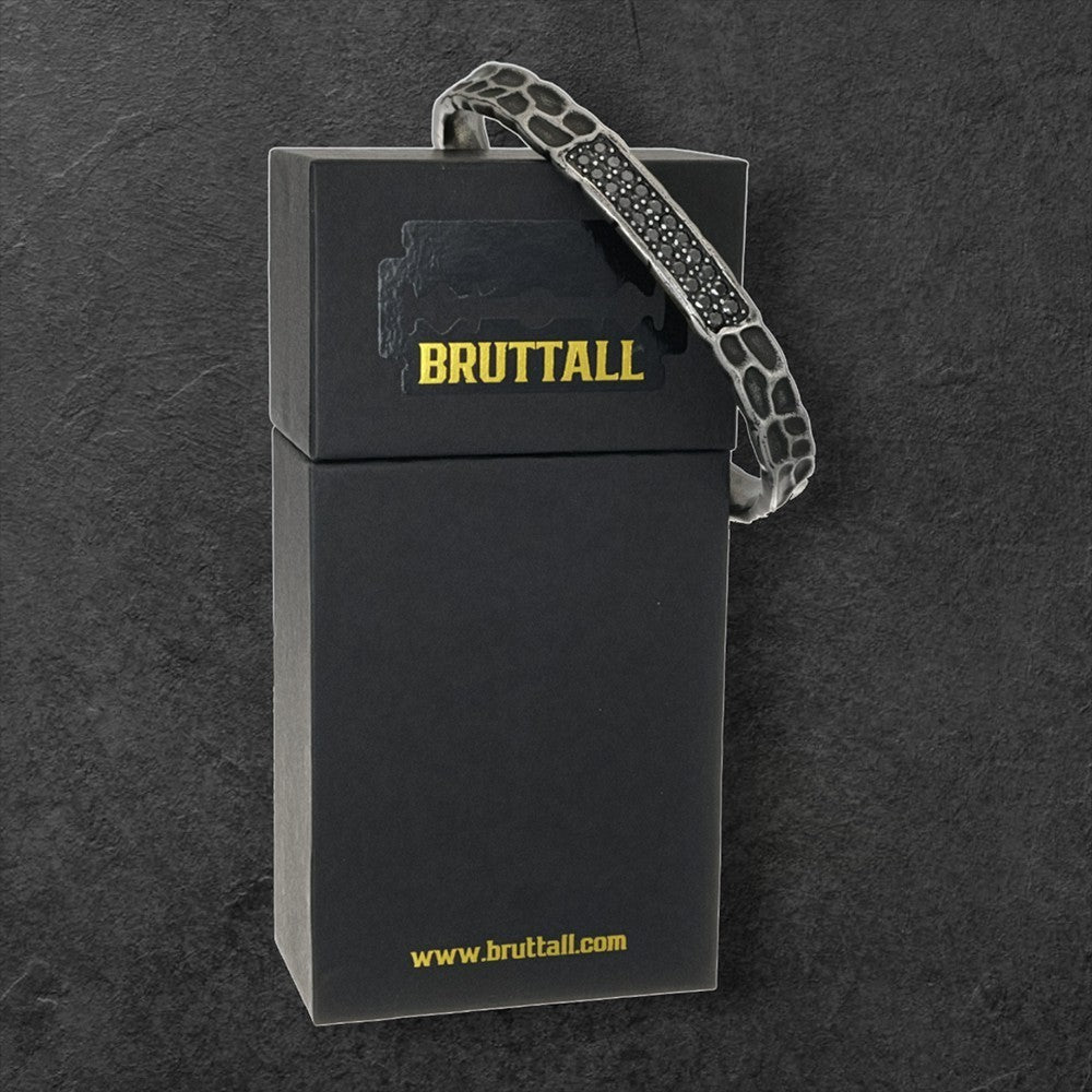 Bruttall RAW bangle in matte gold with textured surface and black Swarovski Zirconia crystals on a black gift box.