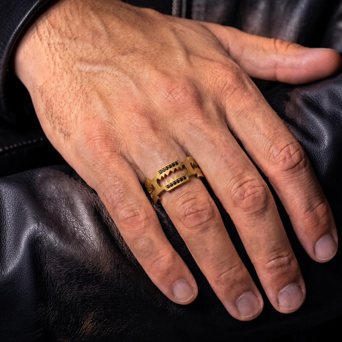 Bruttall RAZOR ring in matte gold plating with black Swarovski Zirconia stones, worn on a hand against leather.