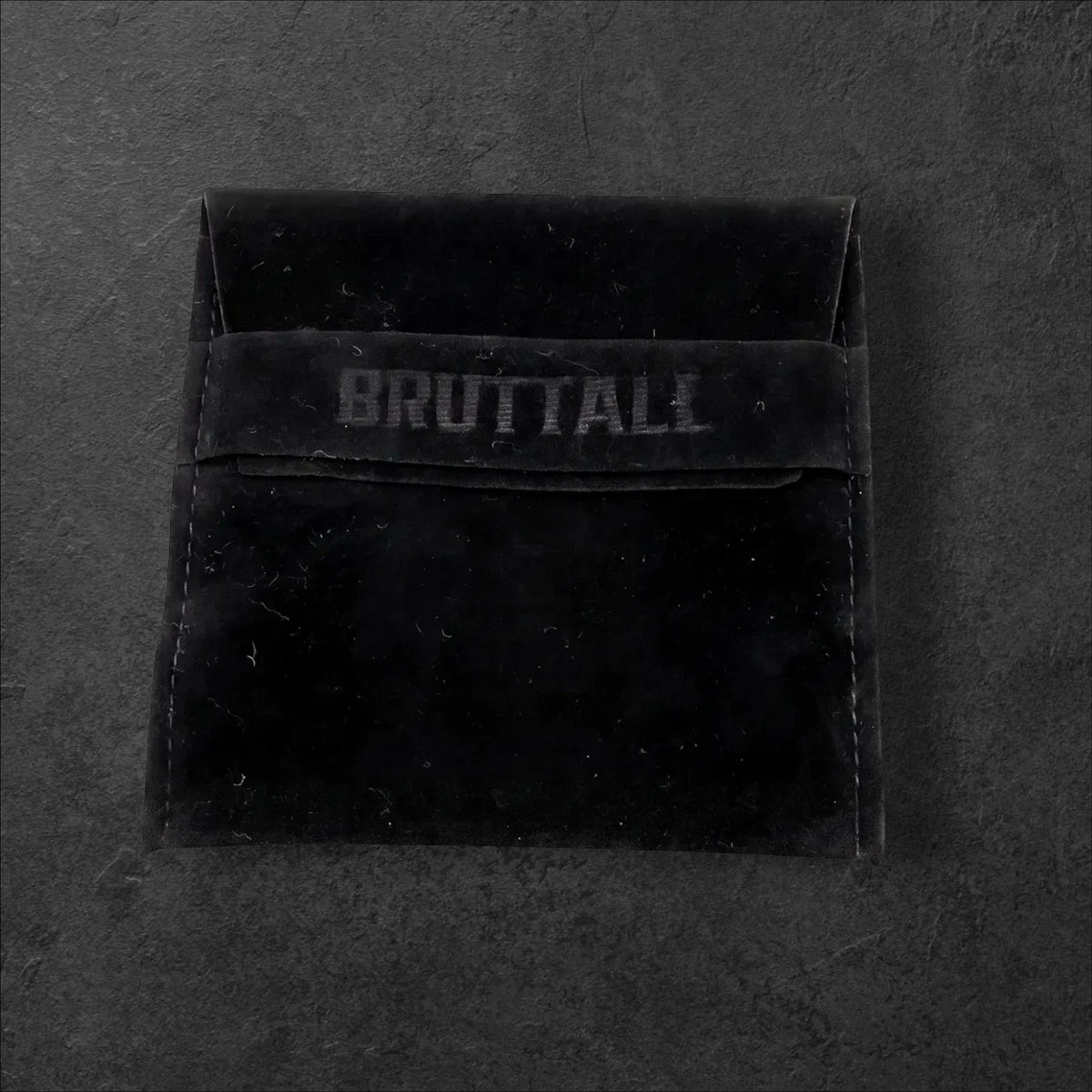 Bruttall branded black velvet jewelry pouch for the TOWER cross earring on a dark textured background