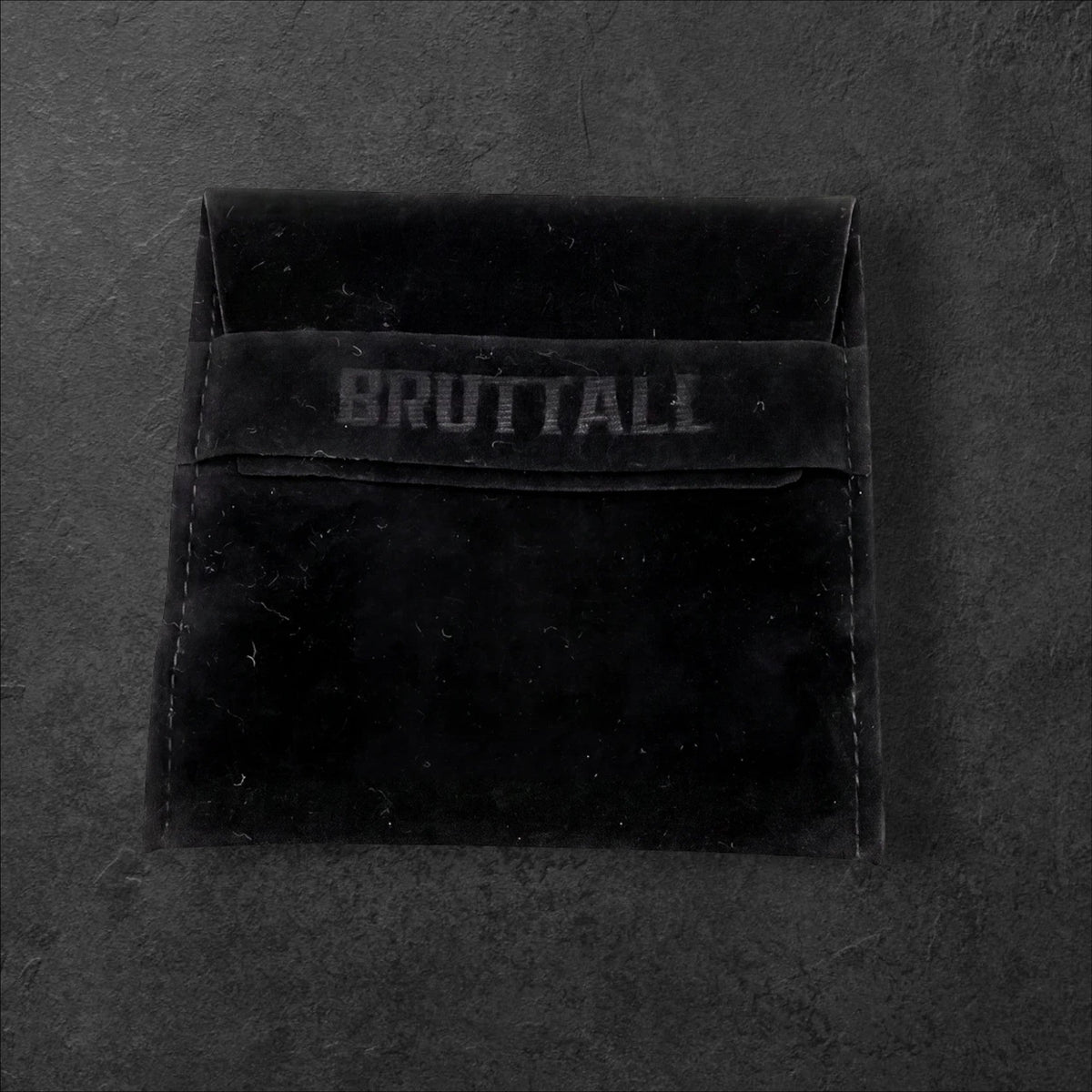 Bruttall branded black velvet jewelry pouch for the RAZOR magnet earring on a dark textured background