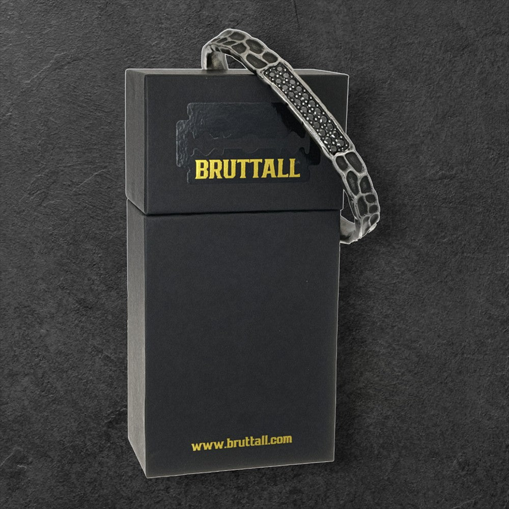Bruttall RAW bangle in antique black with textured surface and embedded Swarovski Zirconia on a black gift box